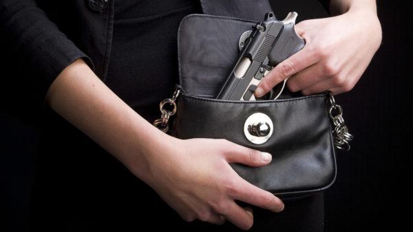 A close-up of a woman holding a handgun in a purse.